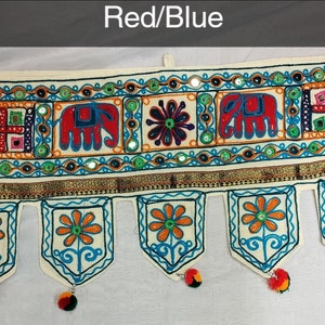 May include: A white fabric door hanging with a red and blue embroidered design. The design features elephants, flowers, and geometric patterns. The hanging has a gold trim and tassels.