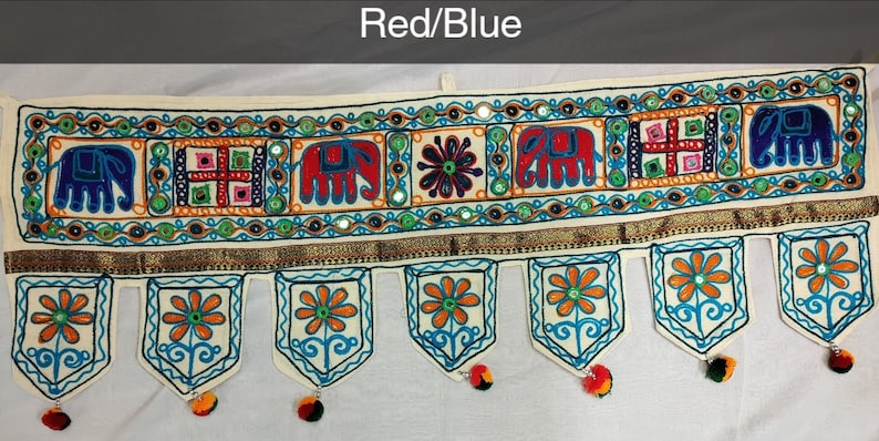 May include: A white fabric door hanging with a red and blue embroidered design. The design features elephants, flowers, and geometric patterns. The hanging has a gold trim and tassels.