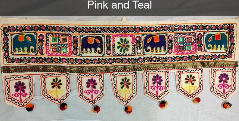 May include: A white cotton door hanging with a pink and teal embroidered design. The design features elephants, flowers, and geometric patterns. The hanging has a fringe border with tassels.