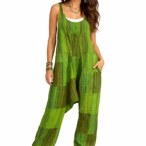May include: Green patchwork jumpsuit with wide legs and a scoop neck. The jumpsuit features a mix of light and dark green vertical stripes. It has pockets and a relaxed fit. The model is wearing a white tank top underneath.