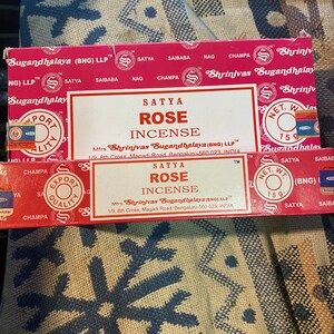May include: Two boxes of Satya Rose incense sticks. The boxes are red with white text and a gold logo. The text on the boxes reads "Satya Rose Incense" and "Mfrs. Shrinivas Sugandhalaya (BNG) LLP".