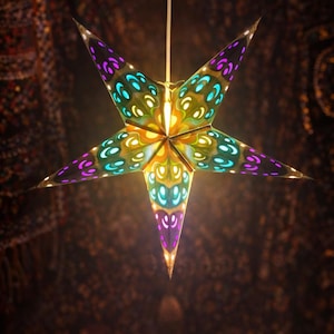 May include: A decorative star-shaped paper lantern with a colorful design. The star has a pointed shape with purple, teal, and yellow accents. The lantern is hanging from a white cord, and the background is dark.