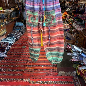 May include: Multicolored striped pants with a drawstring waist and two pockets. The pockets have a circular design with a floral pattern. The pants are made of a soft, lightweight fabric.