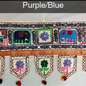 May include: A white fabric door hanging with a colorful embroidered design featuring elephants, flowers, and geometric patterns. The hanging has a purple and blue color scheme and is decorated with small mirrors.