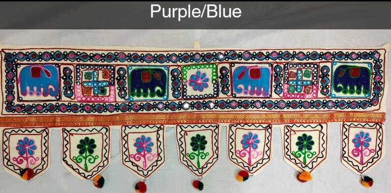May include: A white fabric door hanging with a colorful embroidered design featuring elephants, flowers, and geometric patterns. The hanging has a purple and blue color scheme and is decorated with small mirrors.