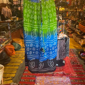 May include: A long, flowing skirt with a tie waist. The skirt is made of a soft, cotton fabric and features a tie-dye pattern in shades of green, blue, and black. The skirt is perfect for a bohemian or hippie look.
