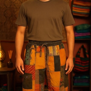 May include: A person wearing a short-sleeved olive green t-shirt and patchwork shorts. The shorts feature a variety of colorful fabric patches in shades of orange, green, and yellow. The shorts have a drawstring waist.