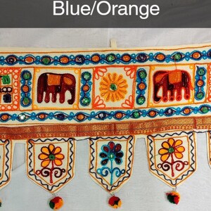 May include: A white fabric door hanging with blue and orange embroidered elephants, flowers, and geometric patterns. The hanging has a scalloped bottom with tassels.