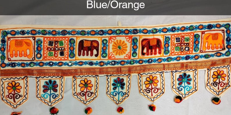 May include: A white fabric door hanging with blue and orange embroidered elephants, flowers, and geometric patterns. The hanging has a scalloped bottom with tassels.