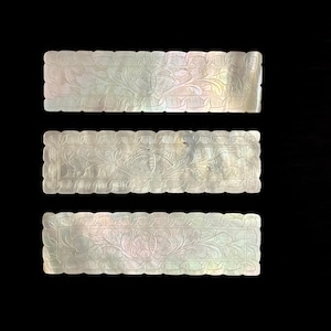 May include: Three rectangular pieces of mother-of-pearl with intricate floral designs carved into the surface.
