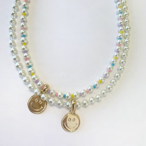 May include: A double-strand pearl necklace with colorful beads and two gold smiley face charms.
