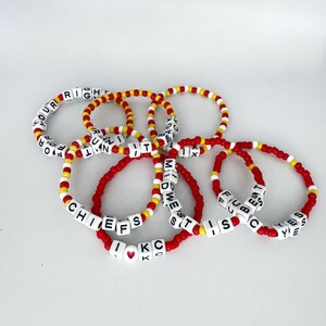 May include: A set of red and yellow beaded bracelets with white letter beads spelling out different phrases, including "Chiefs", "I love KC", "Midwes", "Best", "Yes", "Run It", "Right", "For", and "Fuc".