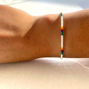 May include: A white beaded bracelet with a rainbow stripe of colored beads.