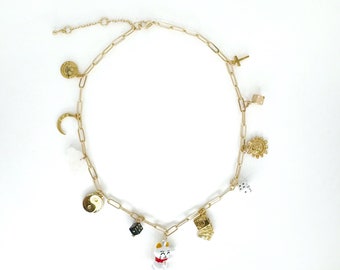 May include: A gold chain necklace with multiple charms, including a crescent moon, a sun, a yin yang symbol, a dice, a cross, a cat, and a playing card.