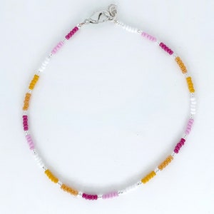 May include: A delicate beaded bracelet with a silver clasp. The bracelet features a repeating pattern of white, pink, and yellow beads.