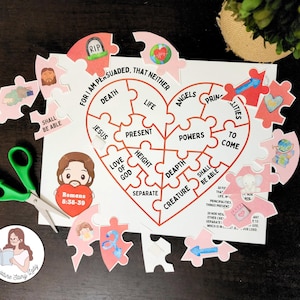 May include: A heart-shaped jigsaw puzzle with religious text and illustrations. The puzzle pieces are pink and white, with phrases like "Jesus" and "Death". Green scissors and a sticker are also visible.