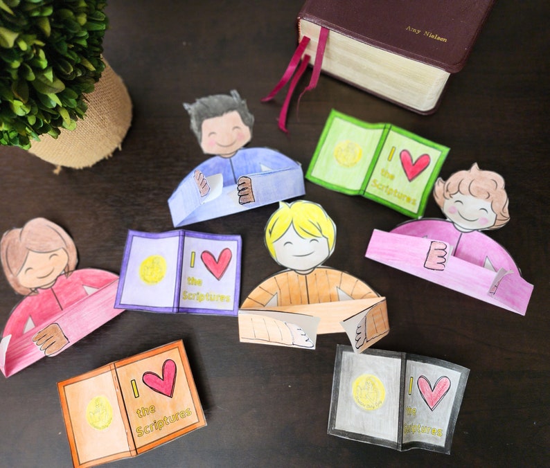 May include: Five paper craft figures of children holding open books with the words "I love the Scriptures" on the cover. The books are in different colors, including green, orange, pink, and blue. The figures are all smiling and have different hair colors.