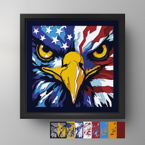 May include: A square framed wall art piece featuring a stylized eagle face with a split design. The left side incorporates blue and white stars, while the right side displays red and white stripes. The eagle has a bright yellow beak and piercing yellow eyes.