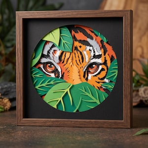 May include: A square wooden frame containing a multi-layered paper art piece. The artwork features a tiger's face with orange, black, and white fur peeking through several layers of green paper leaves within a circular cutout.