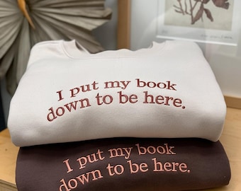 May include: Two sweatshirts with the text "I put my book down to be here."  The top sweatshirt is beige and the bottom sweatshirt is brown.