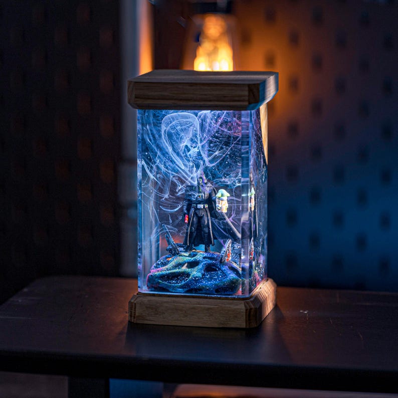 Puede incluir: Una base de l&aacute;mpara de madera con un inserto de resina transparente que contiene una figura de Star Wars. La resina est&aacute; llena de remolinos azules y blancos. La l&aacute;mpara est&aacute; encendida y proyecta un brillo c&aacute;lido.