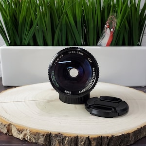 May include: A black camera lens with the text "f=2.8-70 mm 58mm No. 86012083 MULTI-COATED ZOOM AUTO 1:3.5-4.5" printed around the lens.