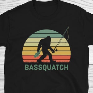 May include: Black t-shirt featuring a retro-style graphic of a Bigfoot holding a fishing rod and a fish. The text "BASSQUATCH" is printed below the graphic.
