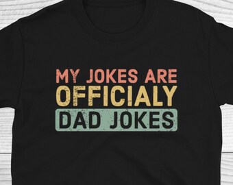 Op de afbeelding: Zwart T-shirt met een vintage-stijl grafische afbeelding met de tekst "Mijn grappen zijn officieel papa-grappen".