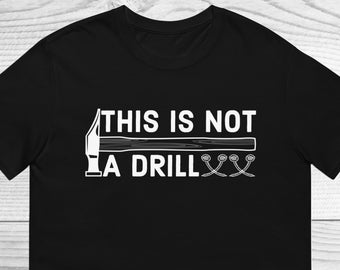 Op de afbeelding: Zwart T-shirt met witte tekst die "Dit is geen oefening" zegt en een afbeelding van een hamer en spijkers.