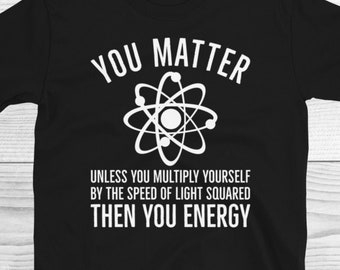 Puede incluir: Camiseta negra con texto blanco que dice "You Matter Unless You Multiply Yourself By The Speed Of Light Squared Then You Energy". El texto está rodeado por un símbolo de átomo blanco.