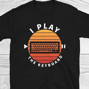 May include: Black t-shirt with a retro-style graphic of a keyboard with the text "I Play The Keyboard".