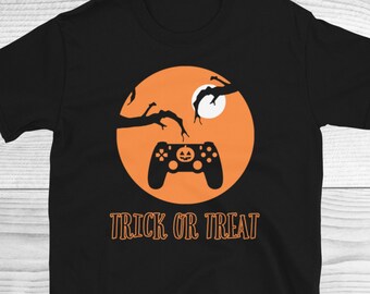 Op de afbeelding: Zwart T-shirt met een oranje afbeelding van een videogamecontroller met een jack-o-lantern erop. De afbeelding is geplaatst tegen een achtergrond van een tak en een volle maan. De tekst "Trick or Treat" staat onder de afbeelding.