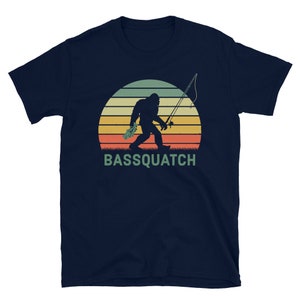 May include: A navy blue t-shirt featuring a retro-style illustration of a Bigfoot holding a fishing rod and a fish. The text "BASSQUATCH" is printed below the illustration.