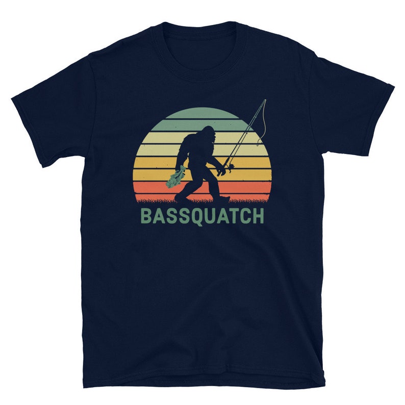 May include: A navy blue t-shirt featuring a retro-style illustration of a Bigfoot holding a fishing rod and a fish. The text "BASSQUATCH" is printed below the illustration.