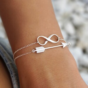 May include: A silver bracelet featuring an infinity symbol charm and an arrow charm.