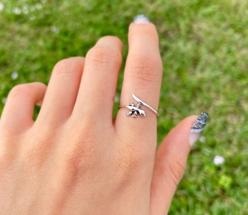 May include: A silver ring with a lizard design. The ring is adjustable and can be worn on any finger.