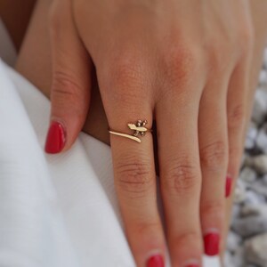 May include: A gold ring with a delicate design of a stylized leaf. The ring is worn on a finger with red nail polish.