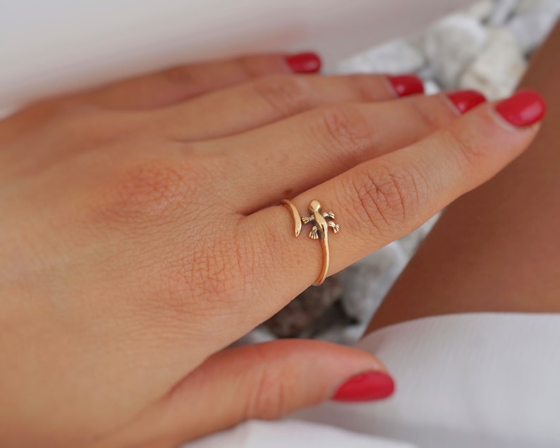 May include: Gold ring with a small lizard design. The ring is wrapped around the finger.