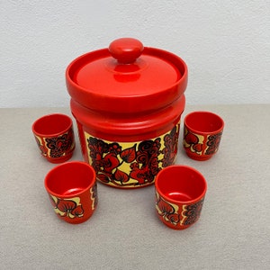 Könnte beinhalten: Ein roter und schwarz gemusterter Eiseimer mit Deckel und vier passenden Schnapsgläsern. Der Eiseimer und die Gläser haben ein florales Design mit schwarzen und gelben Akzenten.