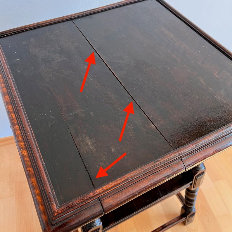 May include: A square wooden side table with a dark brown finish and a visible seam running across the center of the tabletop. Three red arrows point toward the seam, highlighting the gap between the two wooden panels of the table surface.