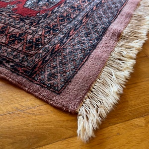 May include: Close-up of a pink and red rug with a black and white geometric pattern. The rug has a fringe border.