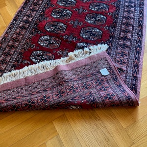 May include: A red and pink rug with a geometric pattern and fringe. The rug is folded in half and the fringe is visible on the bottom edge.