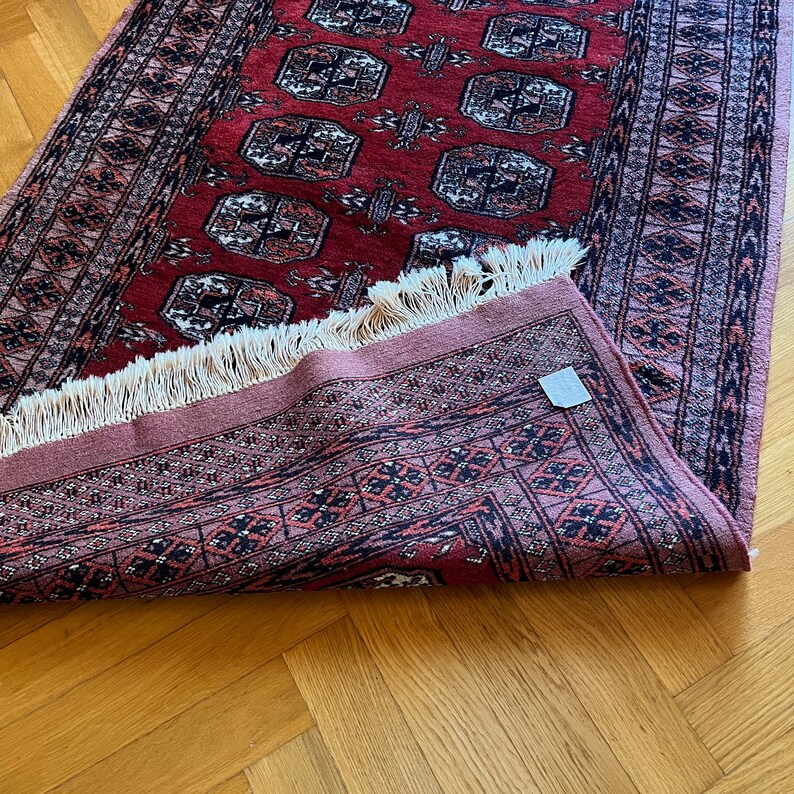 May include: A red and pink rug with a geometric pattern and fringe. The rug is folded in half and the fringe is visible on the bottom edge.