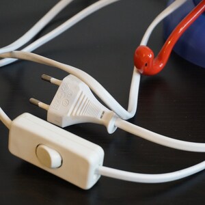 May include: A white electrical cord with a white plug and an inline switch. The cord is connected to a red and blue lamp.