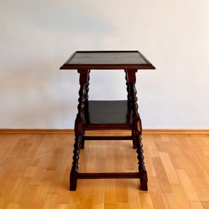 May include: A dark brown wooden side table featuring a square top with a raised edge and a lower square shelf. The table is supported by four turned legs with decorative bulbous detailing and connected by horizontal stretchers at the base.