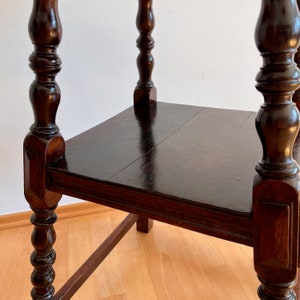 May include: A dark brown wooden side table featuring a square tabletop with a smooth, polished finish. The table is supported by four vertical legs, each characterized by decorative turned wood detailing and a square base section at the corners.