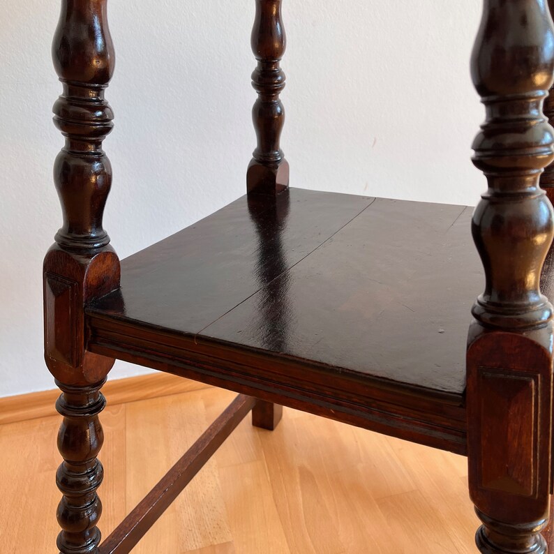 May include: A dark brown wooden side table featuring a square tabletop with a smooth, polished finish. The table is supported by four vertical legs, each characterized by decorative turned wood detailing and a square base section at the corners.