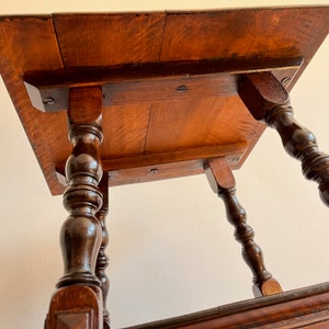 May include: A dark brown wooden side table featuring a square top with visible wood grain and four turned, spindle-style legs. The underside of the tabletop is reinforced with horizontal wooden supports secured by dark metal screws.