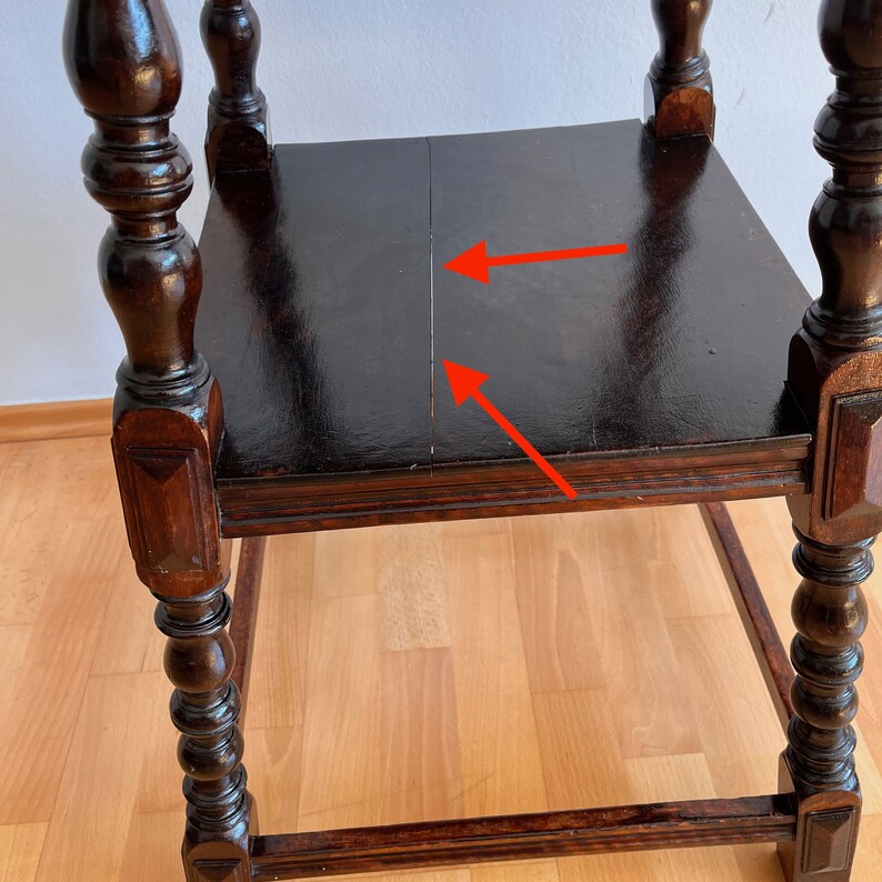 May include: A dark brown wooden side table with turned legs and a square top surface. The top surface features a visible vertical seam running down the center, highlighted by two red arrows pointing toward the gap in the wood grain.