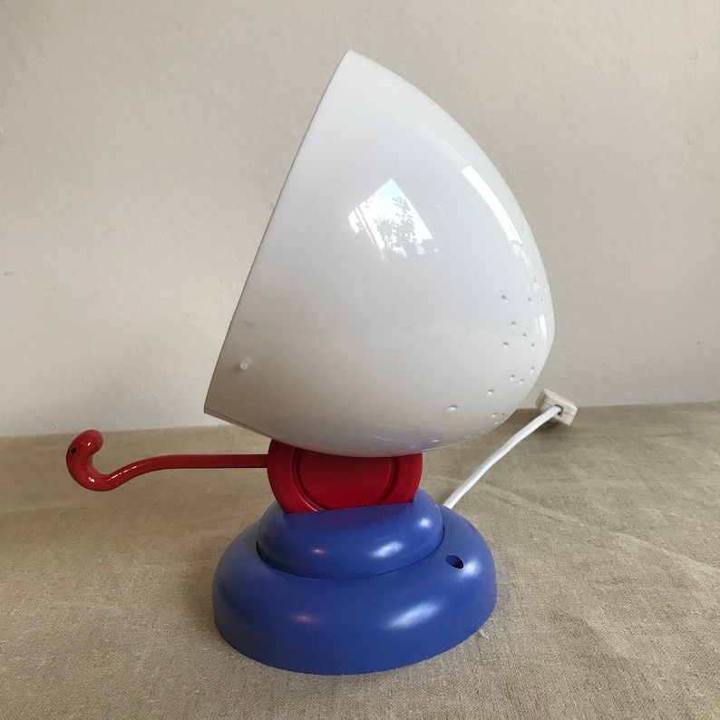 May include: A white lamp with a red and blue base. The lamp has a white cord and a hook on the side.